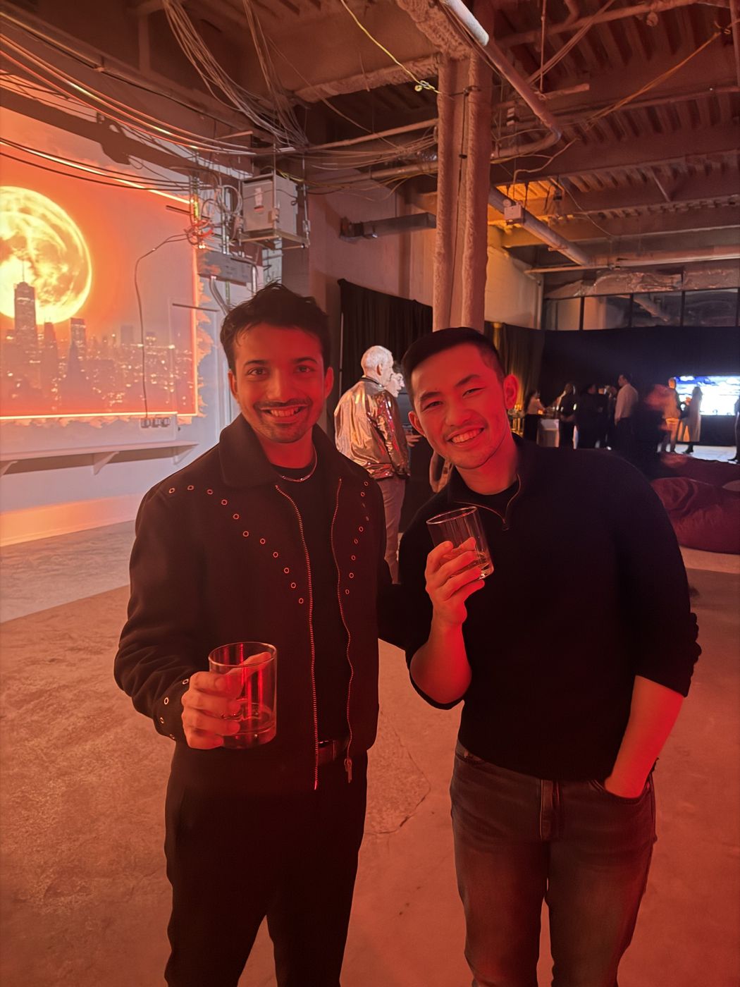 Ashish Dsa with a friend at a New York rooftop gathering, a moonlit skyline glowing behind them